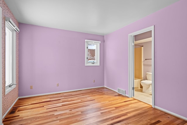 unfurnished bedroom featuring multiple windows, ensuite bath, and light wood-type flooring