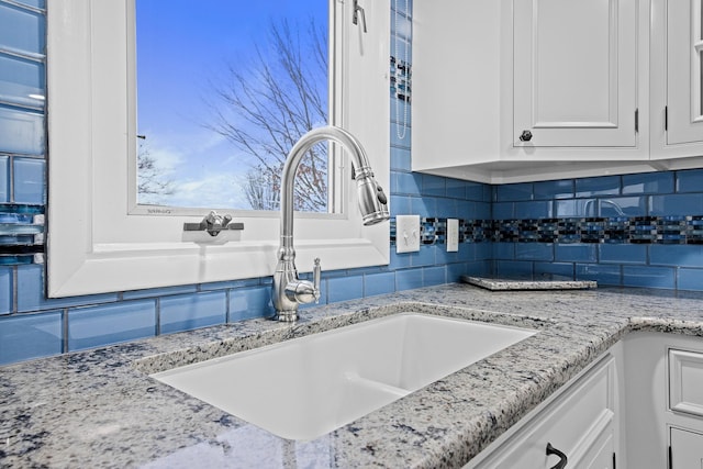 interior details featuring white cabinets, backsplash, light stone counters, and sink