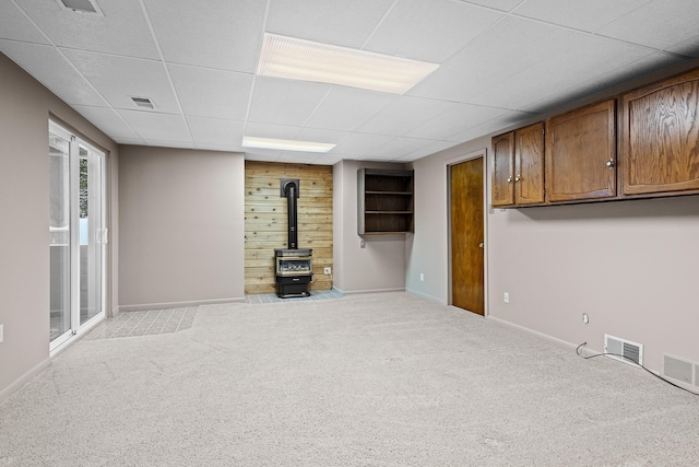 basement with light carpet, a wood stove, a drop ceiling, and wooden walls