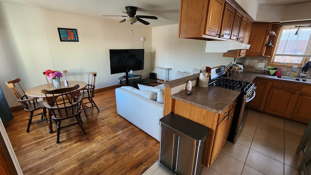 kitchen featuring decorative backsplash, light wood-type flooring, ceiling fan, sink, and stainless steel stove