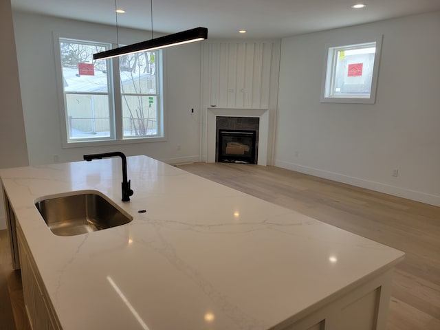 kitchen with light stone countertops, recessed lighting, a sink, a glass covered fireplace, and light wood-type flooring