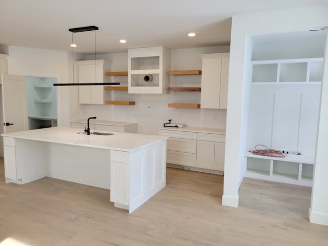 kitchen featuring open shelves, white cabinets, light wood-style floors, pendant lighting, and a sink