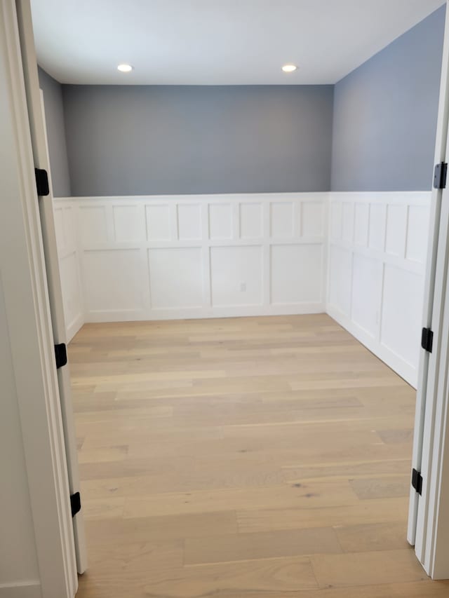 empty room featuring recessed lighting, a wainscoted wall, light wood-style flooring, and a decorative wall