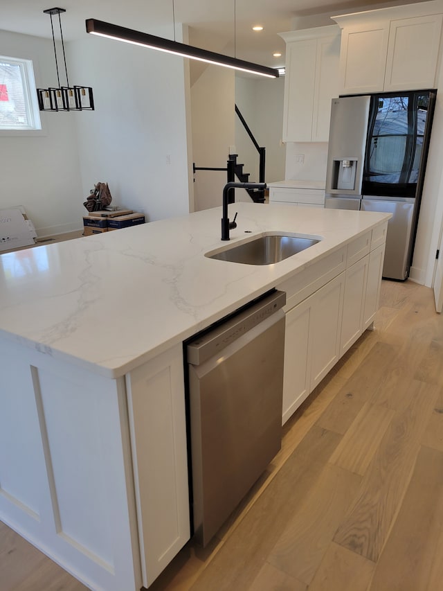 kitchen with light wood-style flooring, a center island with sink, a sink, stainless steel dishwasher, and white cabinets