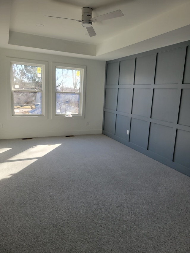 unfurnished bedroom with visible vents, light colored carpet, a raised ceiling, and ceiling fan