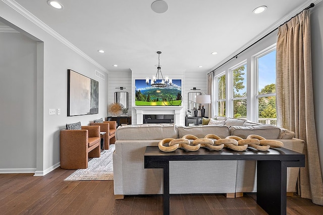 living room featuring wood walls, ornamental molding, dark wood-type flooring, and an inviting chandelier