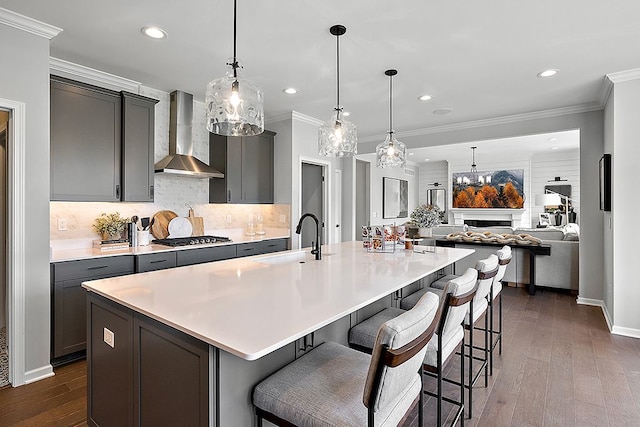 kitchen featuring a large island with sink, sink, wall chimney exhaust hood, and dark hardwood / wood-style flooring