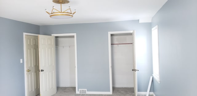 unfurnished bedroom with light carpet, two closets, and multiple windows