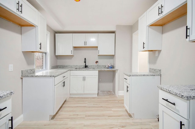 kitchen featuring white cabinets, light stone counters, sink, and light hardwood / wood-style flooring