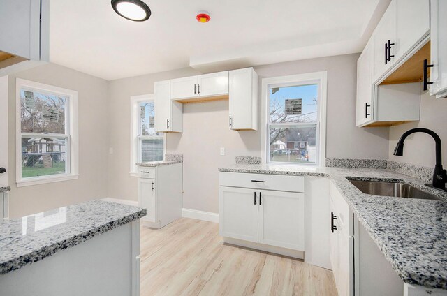 kitchen featuring light stone countertops, sink, white cabinets, and light hardwood / wood-style floors