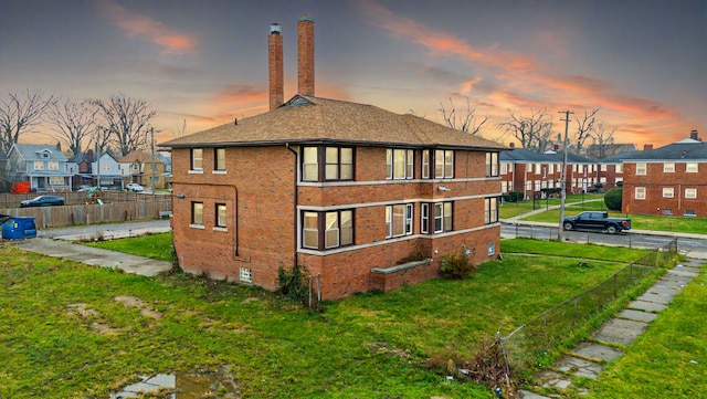 back house at dusk featuring a lawn