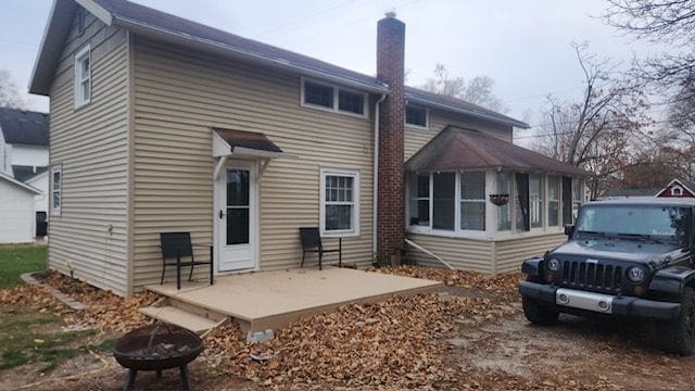 back of property with an outdoor fire pit, a patio area, and a sunroom