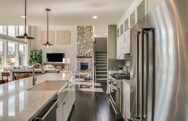 kitchen with light stone counters, pendant lighting, premium appliances, white cabinets, and sink