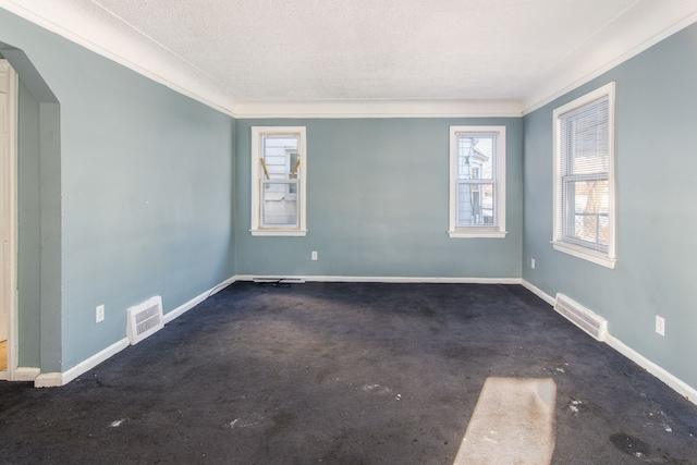 empty room featuring dark carpet, a textured ceiling, and ornamental molding