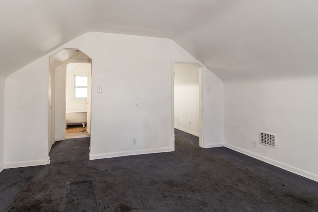 bonus room with dark colored carpet and lofted ceiling