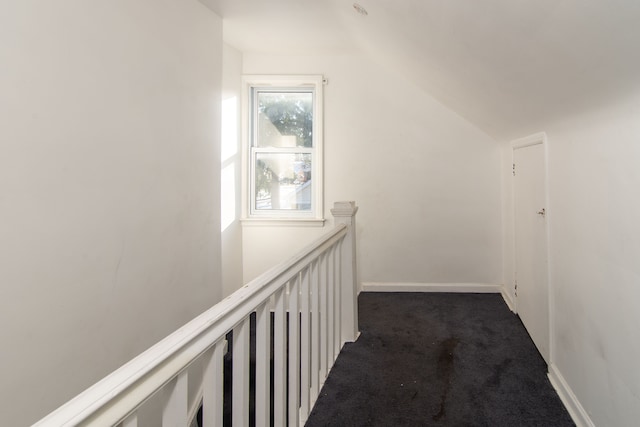 hall with vaulted ceiling and dark colored carpet