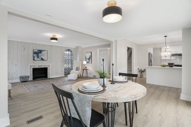 dining space with a fireplace, light hardwood / wood-style floors, an inviting chandelier, and wooden walls