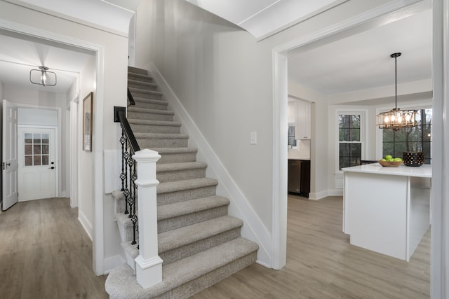 stairs featuring wood-type flooring and a notable chandelier