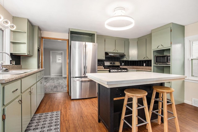 kitchen with light wood-type flooring, tasteful backsplash, stainless steel appliances, sink, and a center island