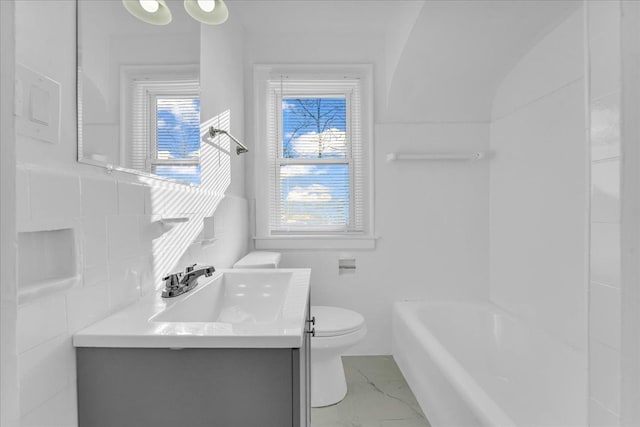 bathroom featuring vanity, a tub to relax in, toilet, and tile walls