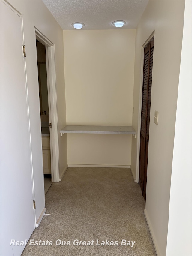 corridor with light colored carpet and a textured ceiling