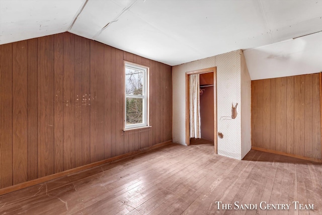 unfurnished bedroom with hardwood / wood-style floors, vaulted ceiling, a closet, and wood walls