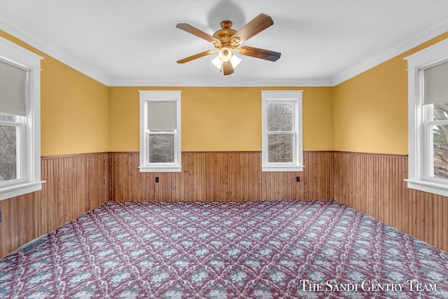 empty room featuring wooden walls, ceiling fan, and ornamental molding