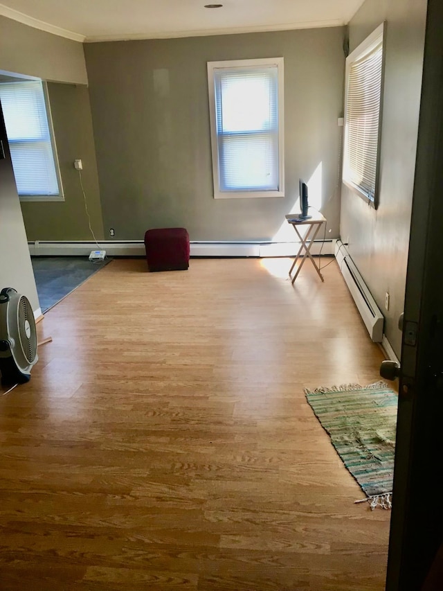 empty room with hardwood / wood-style floors, baseboard heating, and crown molding