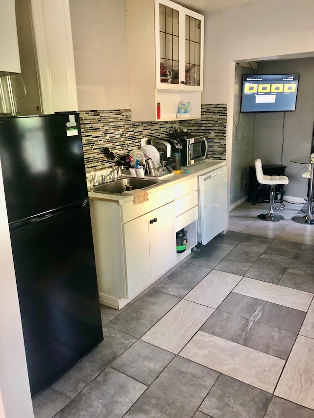 kitchen with backsplash, black fridge, white dishwasher, sink, and white cabinetry