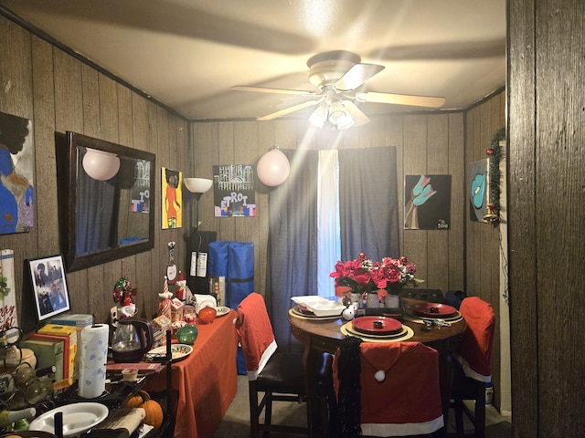 dining space with ceiling fan and wood walls