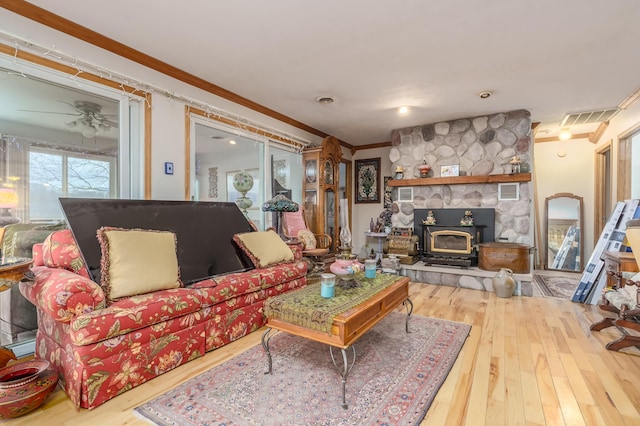 living room with a wood stove, ceiling fan, wood-type flooring, and ornamental molding