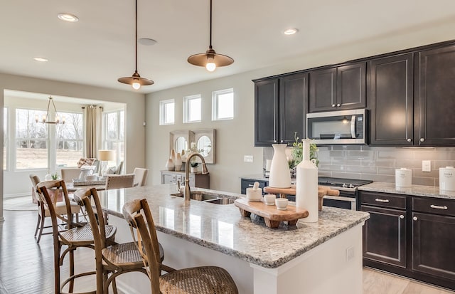 kitchen with light stone counters, an island with sink, sink, and hanging light fixtures