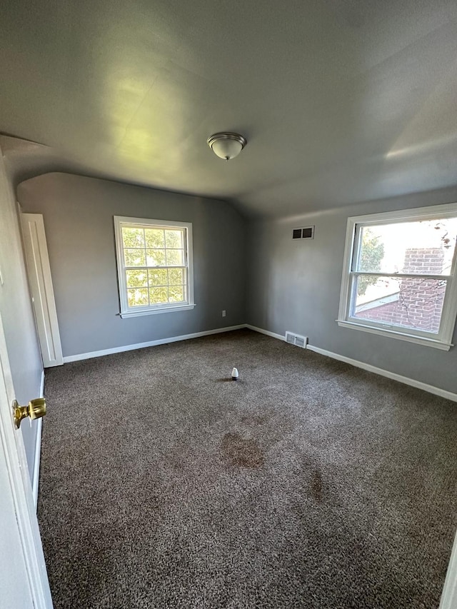 unfurnished room with dark carpet, vaulted ceiling, and a wealth of natural light