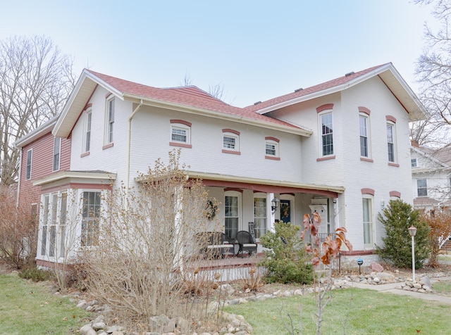 view of front facade with covered porch, a front yard, and brick siding