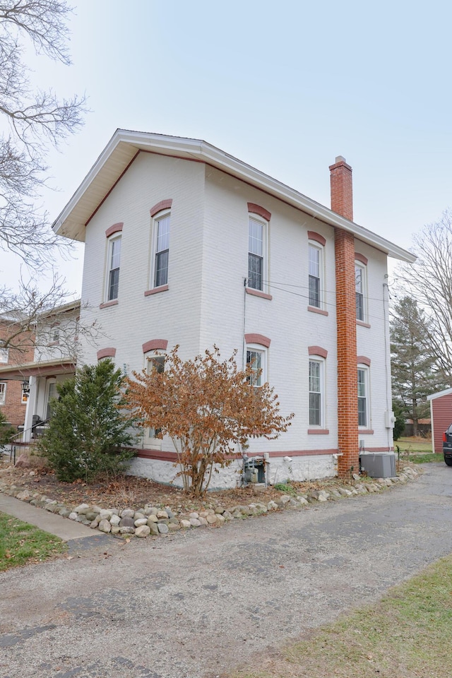 view of home's exterior with a chimney, central AC unit, and brick siding