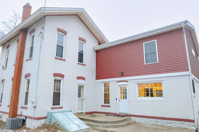 view of front facade featuring brick siding, a chimney, and central air condition unit