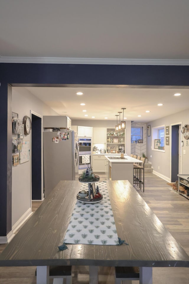 kitchen with a kitchen island with sink, stainless steel appliances, wood finished floors, white cabinets, and decorative light fixtures