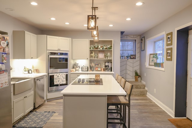 kitchen featuring light wood finished floors, a kitchen island, a breakfast bar area, stainless steel appliances, and light countertops