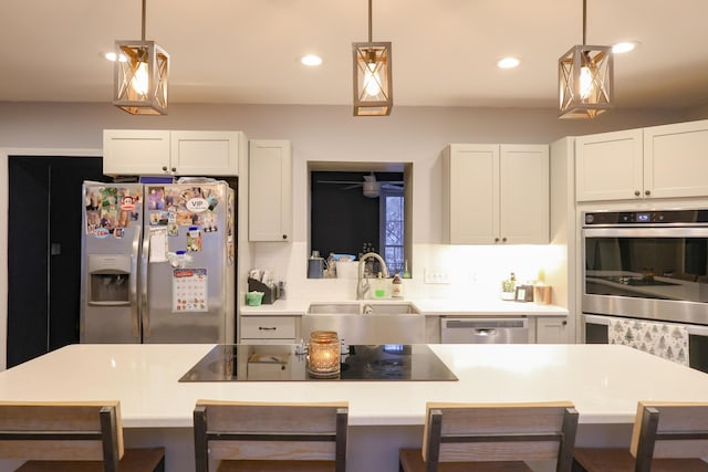 kitchen featuring appliances with stainless steel finishes, a breakfast bar area, a sink, and decorative light fixtures