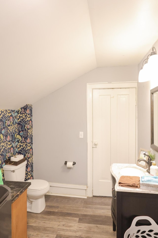 bathroom with toilet, vaulted ceiling, vanity, wood finished floors, and baseboards