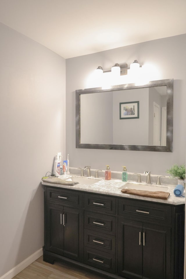 bathroom featuring wood finished floors, a sink, baseboards, and double vanity