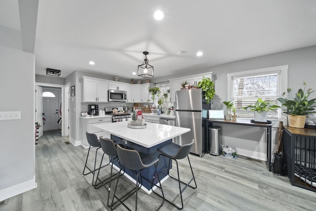 kitchen with a kitchen breakfast bar, light wood-type flooring, decorative light fixtures, white cabinetry, and stainless steel appliances