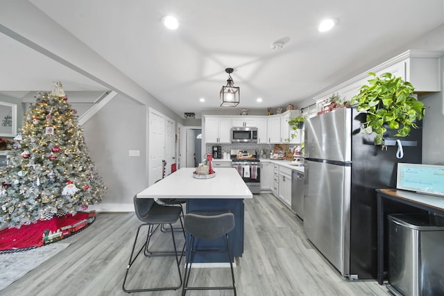 kitchen featuring pendant lighting, tasteful backsplash, light hardwood / wood-style floors, white cabinetry, and stainless steel appliances