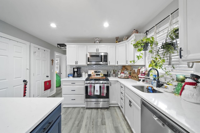 kitchen featuring white cabinetry, sink, light hardwood / wood-style floors, decorative backsplash, and appliances with stainless steel finishes