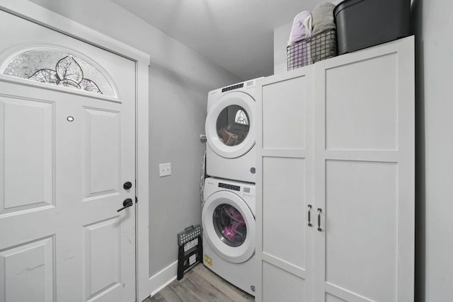 laundry area with stacked washer / dryer, light hardwood / wood-style flooring, and cabinets