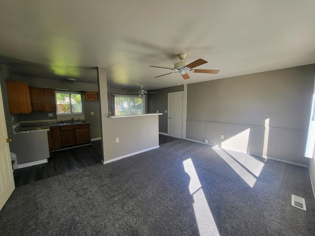 unfurnished living room with ceiling fan, sink, and dark carpet