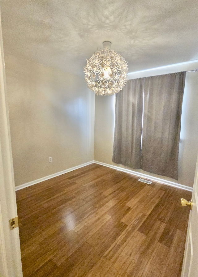 spare room with hardwood / wood-style flooring, a textured ceiling, and a notable chandelier