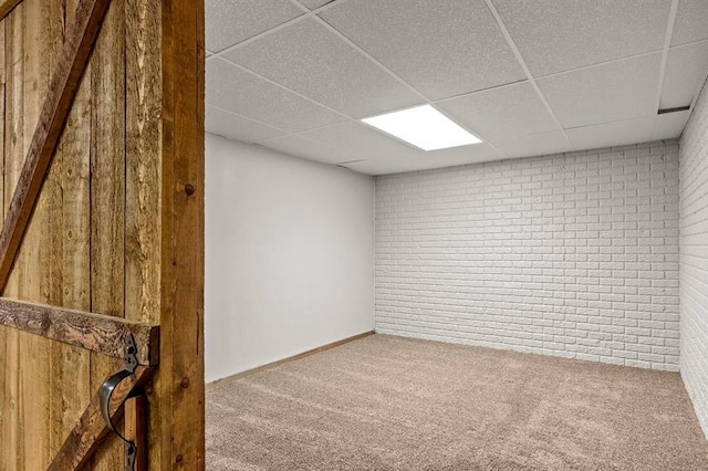 carpeted spare room with a drop ceiling and brick wall