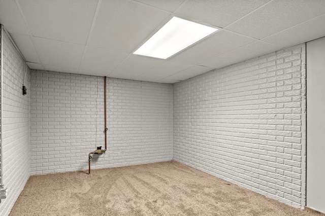 basement with a paneled ceiling, light colored carpet, and brick wall