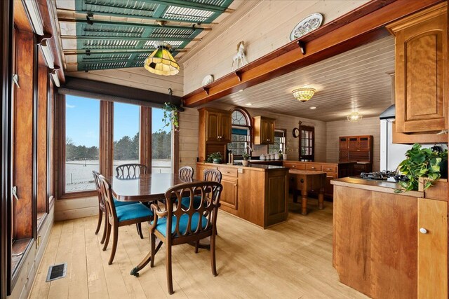 dining area featuring light hardwood / wood-style flooring, a water view, wood ceiling, and wooden walls